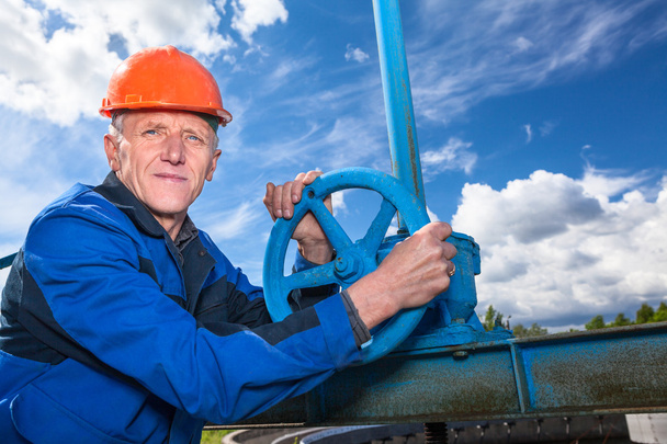 Caucasian mature worker with fitting valve against blue sky - Foto, afbeelding