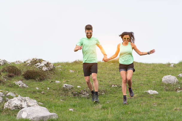 Paar Sportler laufen Hand in Hand über Hügelwiesen - Foto, Bild