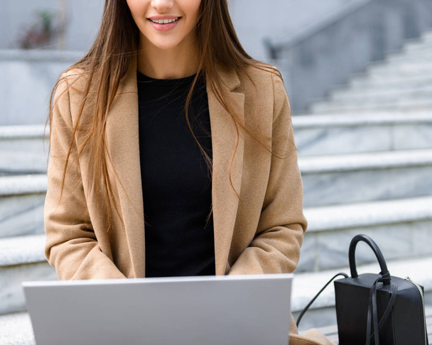 Beautiful young woman wearing autumn coat using laptop - Фото, зображення
