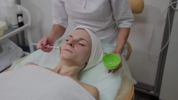 Professionele cosmetoloog zet een masker op de patiënten gezicht. - Video