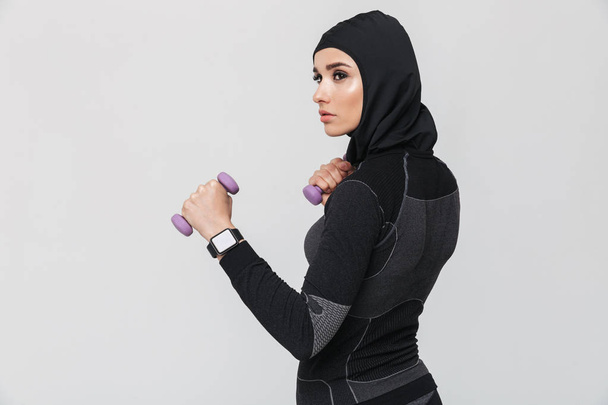Young woman fitness muslim make exercises with dumbbells isolated over white wall background. - Fotoğraf, Görsel
