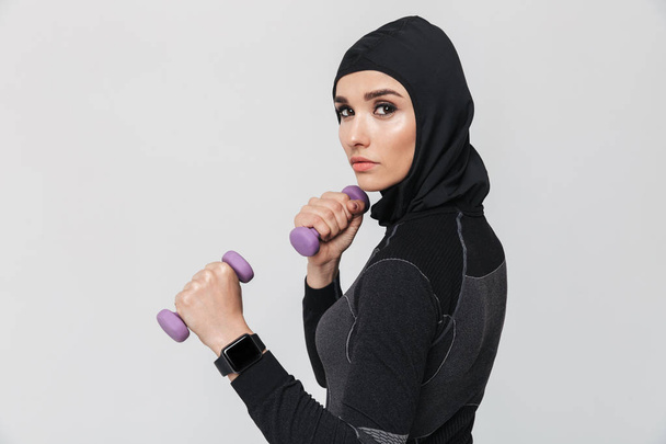Young woman fitness muslim make exercises with dumbbells isolated over white wall background. - Photo, Image