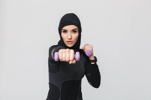 Nuori nainen kunto muslimi tehdä harjoituksia käsipainoilla eristetty yli valkoinen seinä tausta
. - Valokuva, kuva