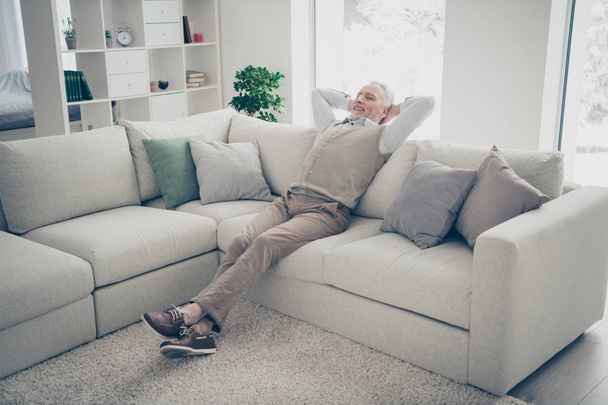 Full length body size photo amazing he him his aged man overjoyed calm hands arms behind head day off imaginary flight wear white shirt waistcoat pants sit cozy divan flat house living room indoors - 写真・画像