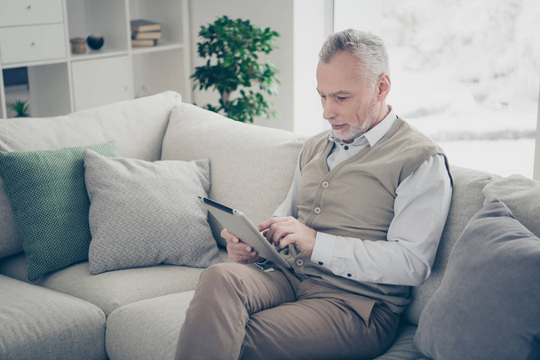 Close up side profile photo amazing he him his aged man hands arms e-book search look browsing information novelty wear white shirt waistcoat pants sit cozy divan flat house living room indoors - Φωτογραφία, εικόνα