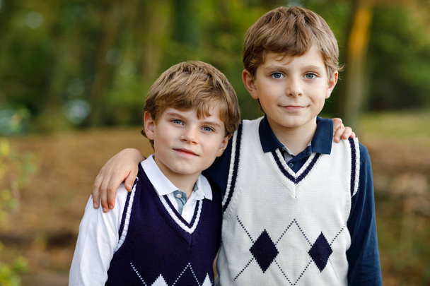 Portret van een kleine school kids jongens zitten in bos. Gelukkige kinderen, beste vrienden en broers en zussen plezier op warme zonnige dag begin van de herfst. Twins en familie, natuur en actieve recreatie. - Foto, afbeelding