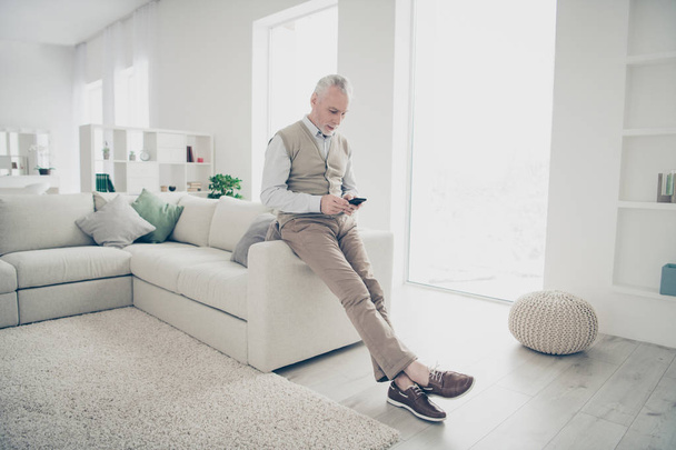 Full length body size photo amazing manager he him his aged man arms hands telephone reader email wear white shirt waistcoat pants stand near cozy comfort divan bright flat house living room indoors - Foto, afbeelding