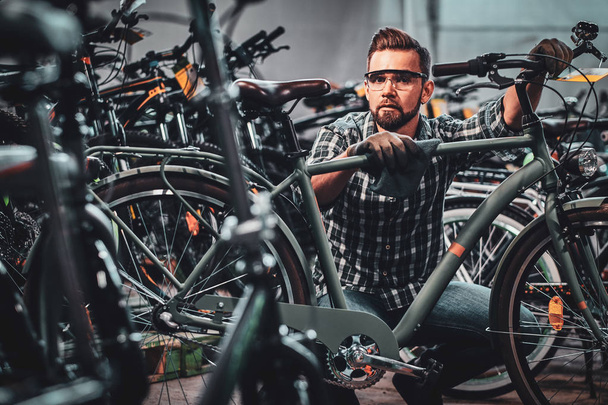 Πολυάσχολος ελκυστικός άνθρωπος με προστατευτικά γυαλιά καθαρίζει το ποδήλατο από τη βρωμιά - Φωτογραφία, εικόνα