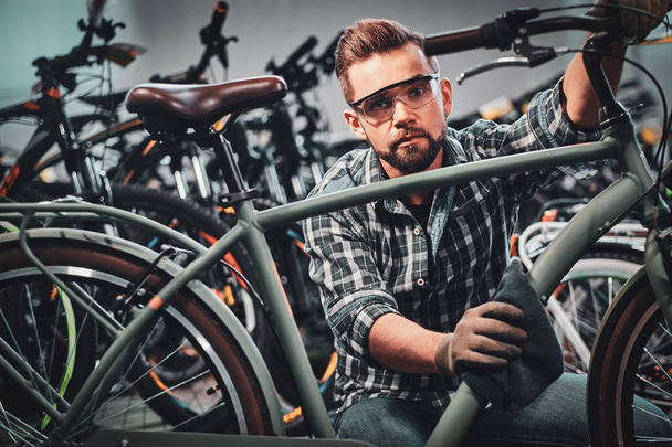 Ocupado homem atraente em óculos de proteção está limpando a bicicleta da sujeira
 - Foto, Imagem