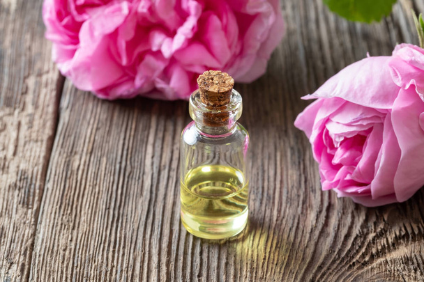 Een fles rose etherische olie met roze bloemen - Foto, afbeelding