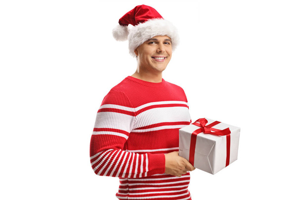 Young man wearing a santa claus hat and holding a christmas gift box isolated on white background - Φωτογραφία, εικόνα
