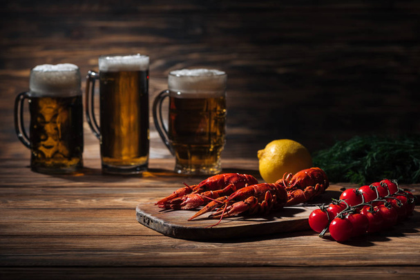 selective focus of red lobsters, tomatoes, dill, lemon and glasses with beer on wooden surface - Photo, Image