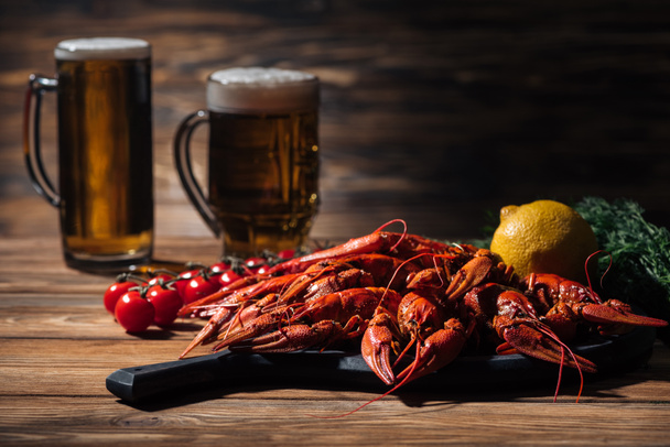 red lobsters, tomatoes, dill, lemon and glasses with beer on wooden surface - Foto, Bild