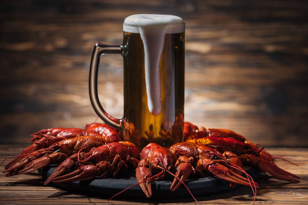 glass with beer and foam on plate with red lobsters at wooden surface - Foto, imagen