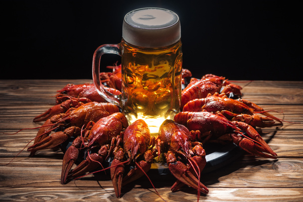 glass with beer and foam on plate with red lobsters at wooden surface - Photo, Image