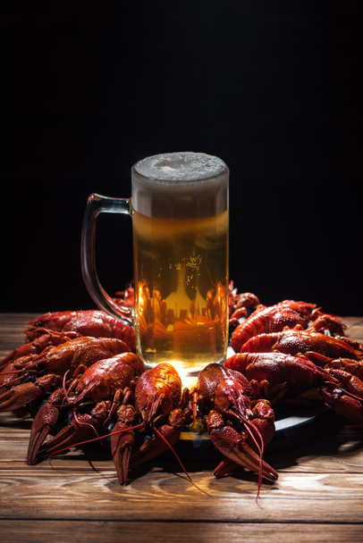 glass with beer and foam on plate with red lobsters at wooden surface - Фото, зображення