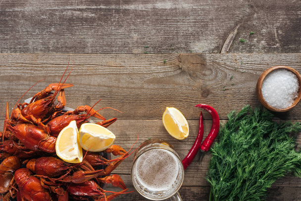 top view of red lobsters, dill, lemon slices, pepper, glasses with beer and salt on wooden surface - Fotografie, Obrázek