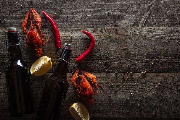 top view of red lobsters, lemon slices, pepper and bottles with beer on wooden surface - Foto, Imagem