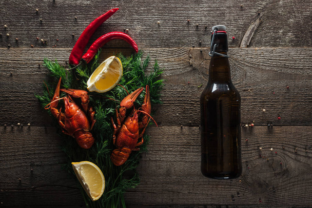top view of red lobsters, lemon slices, dill, pepper and bottle with beer on wooden surface - Photo, Image