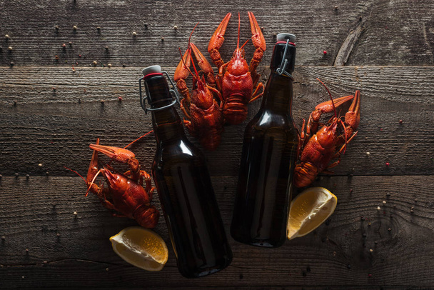top view of red lobsters, lemon slices and bottles with beer on wooden surface - Foto, Imagem