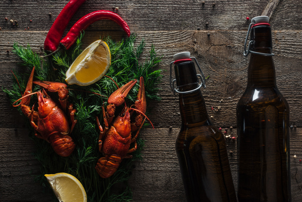Κορυφαία θέα των κόκκινων αστακών, φέτες λεμονιού, άνηθο, πιπέρι και μπουκάλια με μπύρα σε ξύλινη επιφάνεια - Φωτογραφία, εικόνα