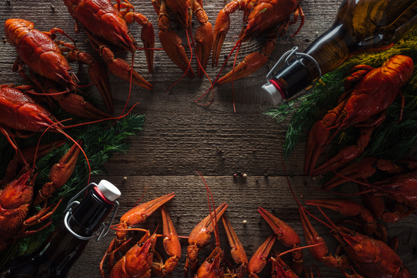 top view of red lobsters, dill and glass bottles with beer on wooden surface - Photo, Image