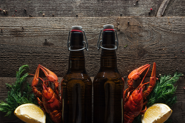 top view of red lobsters, dill, lemon slices and glass bottles with beer on wooden surface - Фото, изображение