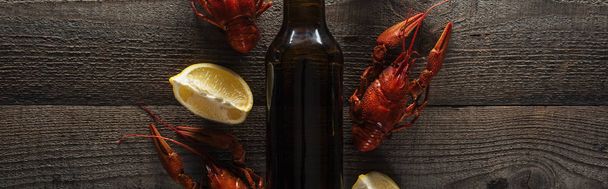 plano panorámico de langostas rojas, rodajas de limón y botella de vidrio con cerveza en la superficie de madera
 - Foto, Imagen