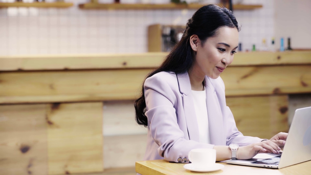 усміхнена і красива азіатська бізнес-леді в костюмі використовує ноутбук в кафе
  - Кадри, відео