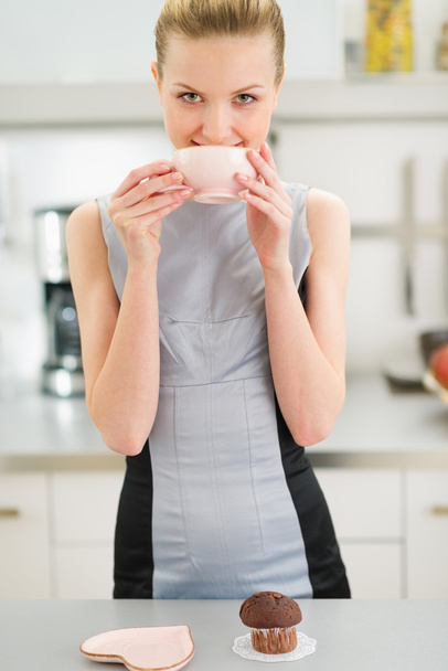 Happy young housewife drinking tea with chocolate muffin - Zdjęcie, obraz