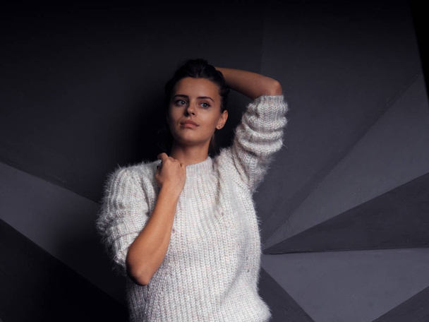 portrait of beautiful young woman in white sweater in front of black wall - Fotó, kép