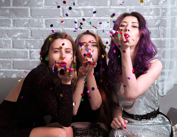 портрет красивых молодых женщин в платьях, дующих конфетти в камеру
 - Фото, изображение