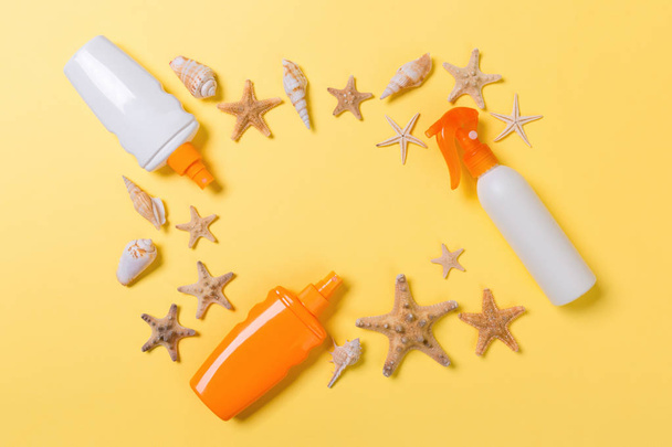 sunscreen cream with starfish and seashells in bottles on yellow background, top view - Foto, Bild