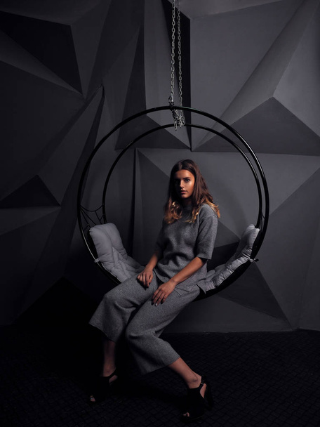 portrait of beautiful young woman in grey wool overall in front of black wall - Foto, imagen