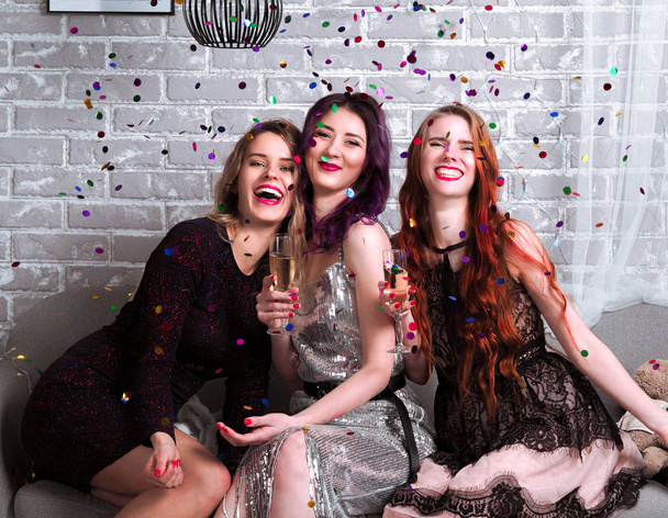 portrait of beautiful young women in dresses with champagne and confetti in front of brick wall - Photo, Image