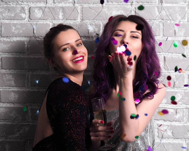 portrét krásných mladých žen v šatech se šampaňským a konfety před cihlovou stěnou - Fotografie, Obrázek