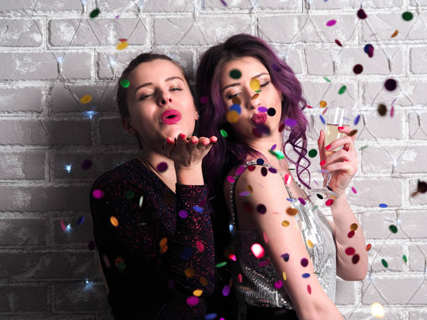 portrait of beautiful young women in dresses with champagne and confetti in front of brick wall - Fotoğraf, Görsel