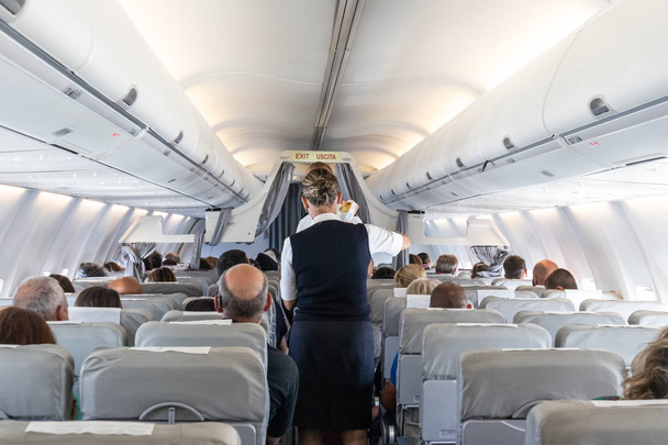 Wnętrze samolotu użytkowego ze stewardesą obsługującą pasażerów na siedzeniach podczas lotu. - Zdjęcie, obraz