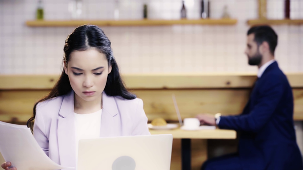 mulher de negócios séria olhando para papéis e tela do laptop, empresário digitando no computador e beber café no fundo
  - Filmagem, Vídeo