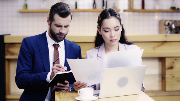 hombre de negocios escribiendo en cuaderno y discutiendo papeles con la mujer de negocios, mirando la pantalla del ordenador portátil
  - Imágenes, Vídeo