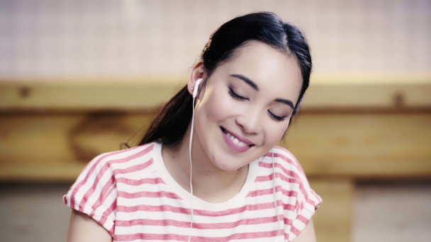 lächelnde und hübsche Asiatin im T-Shirt, die im Café Musik hört  - Filmmaterial, Video
