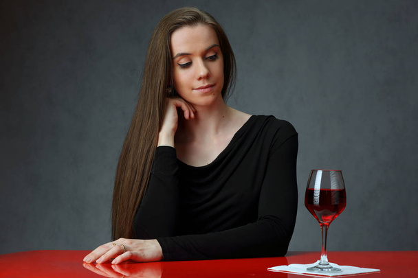 Cute girl at the red table with a glass of wine - Фото, зображення