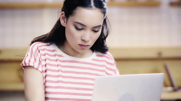 серйозна азіатська жінка в футболці, що пише в блокноті і використовує ноутбук в кафе
  - Кадри, відео