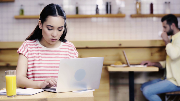 азіатська жінка в футболці, що пише в блокноті і друкує на ноутбуці, чоловік використовує комп'ютер і п'є каву на фоні
  - Кадри, відео