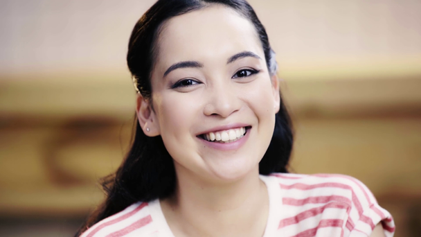 attraktive, brünette, asiatische Frau blickt in die Kamera und lächelt im Café  - Filmmaterial, Video