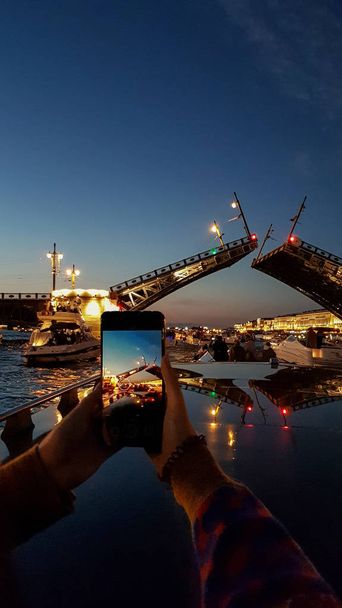 Menina tira foto no telefone reprodução Palace Bridge em São Petersburgo durante Noites Brancas. Vista do rio Neva para a ponte elevada. São Petersburgo, Rússia
 - Foto, Imagem
