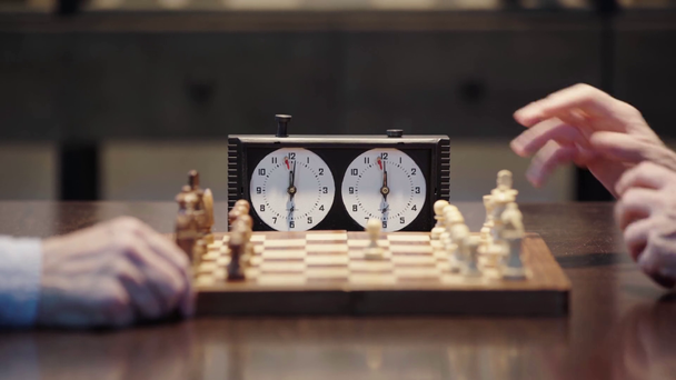 vista cortada de dois homens seniores jogando xadrez e pressionando o botão no relógio de xadrez na mesa
  - Filmagem, Vídeo