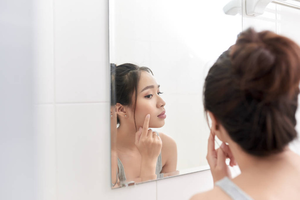 Cura della pelle. Donna che applica la crema per la pelle sul viso davanti allo specchio
 - Foto, immagini