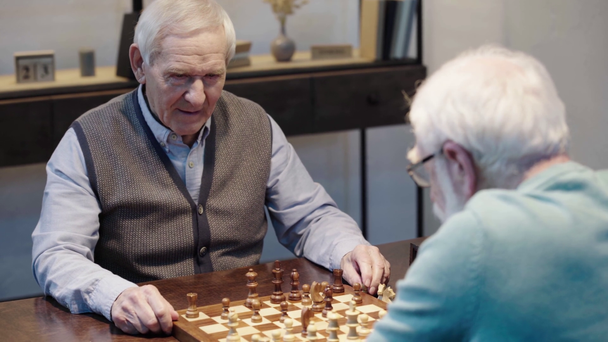 hombre mayor hablando mientras juega al ajedrez con un amigo y presionando el botón en el reloj de ajedrez en la mesa
 - Imágenes, Vídeo