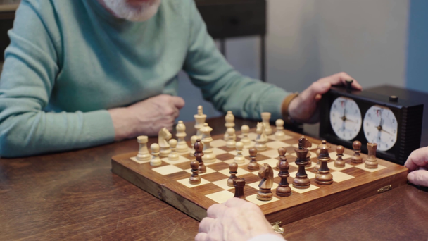 vista parcial de dos hombres mayores jugando al ajedrez y presionando el botón en el reloj de ajedrez en la mesa
 - Metraje, vídeo